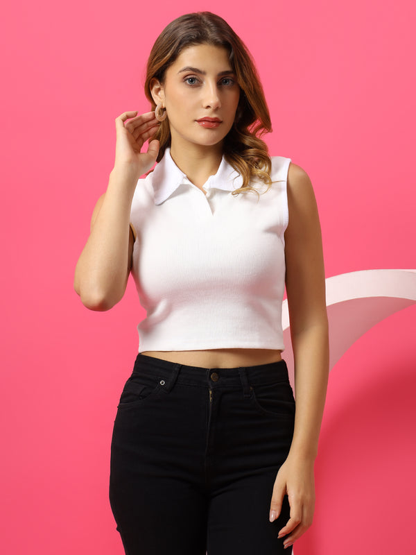 Woman wearing a white sleeveless polo shirt and black pants against a pink background
